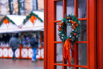 Christmas fair rainy day time festive December Europe holidays season with blurred background of bokeh light and people silhouette, foreground focus on classic red telephone cabin object