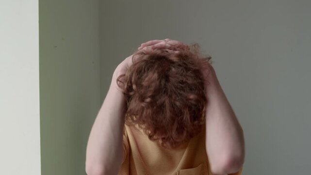 Chest up shot of young Caucasian man in plain mustard t-shirt stretching neck after sedentary work indoors