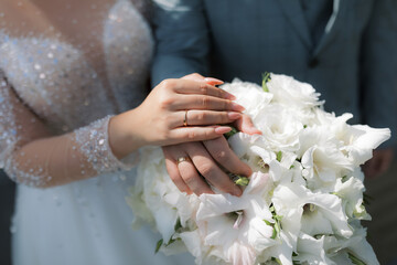 A pair of hands with wedding rings against a background of white flowers.