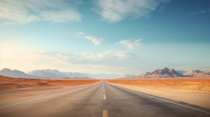 Naklejka premium A long, straight road stretches through a vast desert landscape under a clear blue sky.