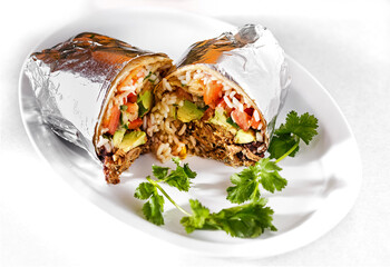Beef burrito cut in half wrapped in aluminum foil in a white plate with parsley garnish