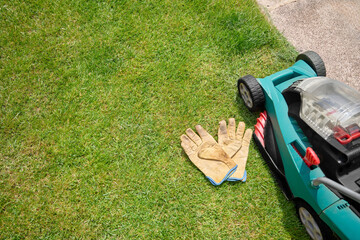 Electric lawnmower with rechargeable battery along with gardening gloves on the grass in the...