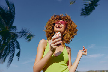 Young woman enjoying ice cream under a blue sky with palm trees