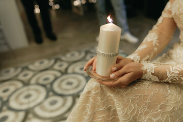 Women's hands hold a candle at a wedding, wedding traditions and customs &lsquo;Passing the Hearth&rsquo;.