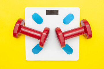 Red dumbbells on floor scales close up on yellow background