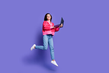 Full length photo of charming positive woman wear pink cardigan jumping reading modern gadget empty space isolated purple color background © deagreez
