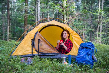 A young girl is relaxing in a tent in a clearing.