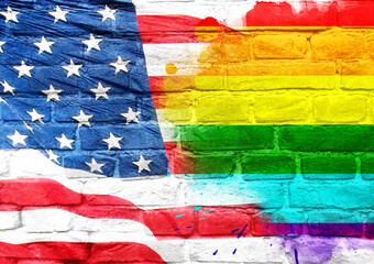 A colorful rainbow flag is painted on a brick wall next to the American flag