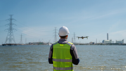 Engineer in a safety vest operating a drone to inspect and survey electrical power lines....