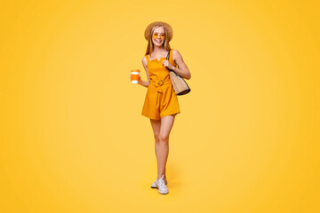 Full-Length Portrait Of Beautiful Teen Girl In Summer Clothes With Drink In Hand Posing Over Yellow Background In Studio, Free Space
