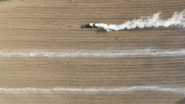 Aerial view of a tractor spreading lime on agricultural fields to improve soil quality after the autumn harvest. The use of lime powder to neutralize the acidity of the soil