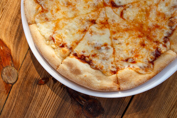 Juicy cheese pizza on a white plate on a wooden table.