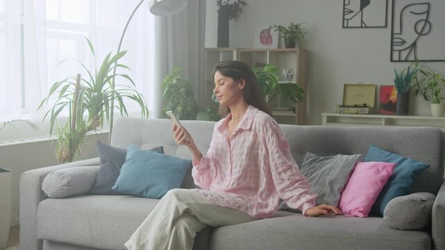 Relaxed woman on sofa using smartphone in cozy living room
