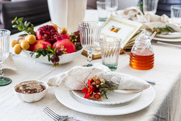Jewish holiday Rosh Hashana festive table setting with plate, honey, apple ,pomegranates, dates, book of hebrew prayers, kiddush cup