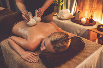 Hot herbal ball spa massage body treatment, masseur gently compresses herb bag on woman body....