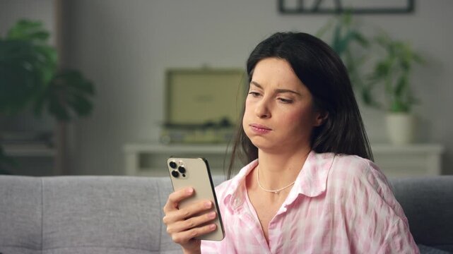 Woman reacting with concern to news on smartphone on couch