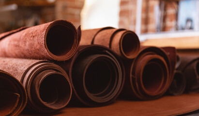 Different brown rolls of natural color leather on rack in workshop. Materials for footwear and DIY handmade craft product
