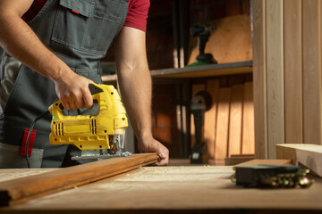 A skilled craftsman is focused on his woodworking project, using a electric jigsaw to cut timber precisely. The workshop is well-organized, with various tools and materials surrounding him, showcasing