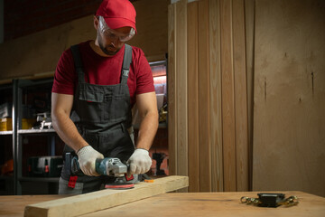 An experienced craftsman focuses on processing a piece of wood in a well-equipped workshop using a...