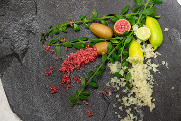 Ripe yellow and burgundy oblong citrus fruits with green sprigs on the black slate slab, close-up. Australian finger lime plant indoor growing. Microcitrus australasica, Faustrimedin