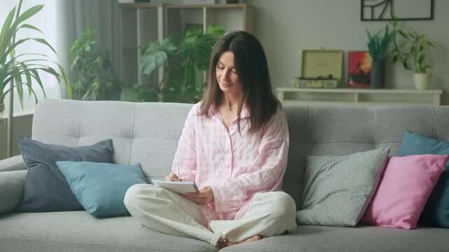 Relaxing woman journaling on cozy couch in plant-filled living room