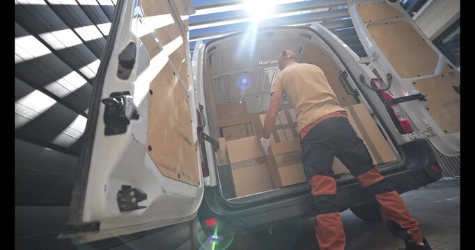 Delivery Worker Loading Packages Into a Van at a Warehouse During Daylight Hours