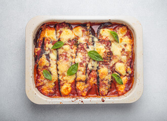 Eggplant parmigiana di melanzane freshly baked and decorated with basil leaves, resting in a baking pan. Classic italian dish