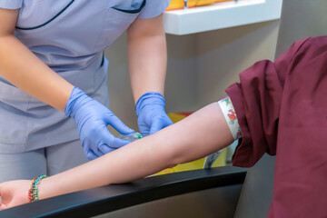 Nurse taking blood sample from young female patient in the background. Selective focus on sample...
