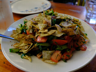 Fattoush salad on a white plate, featuring fresh vegetables like tomatoes, cucumbers, and parsley, seasoned with spices and topped with crispy pita chips.