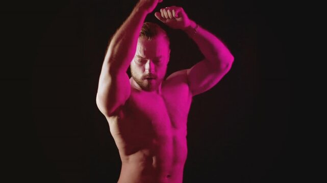 Dark video of a young blonde bearded caucasian man dancing with pink light in slow motion. Fashion trendy studio videoclip gogo dancer isolated with black background