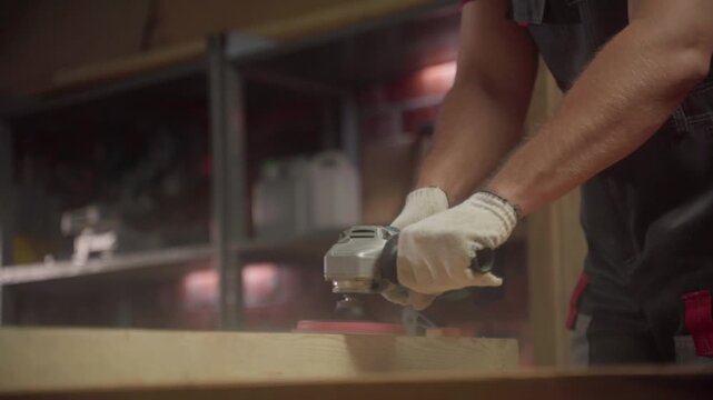 The master works hard in the workshop, paying special attention to the treatment of the wooden surface with a grinding power tool. The warm light of the evening lighting creates a cozy atmosphere when