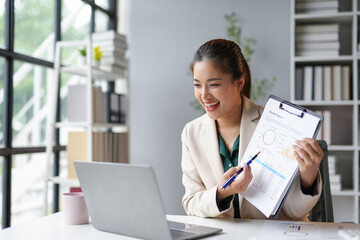 Smiling businesswoman discussing monthly report using graphs during video call on laptop in the office