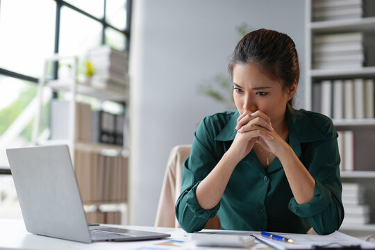Young businesswoman is holding her hands together in front of her mouth, looking worried while working at her desk