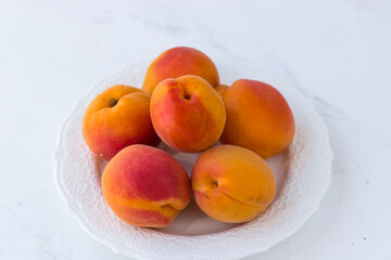 Juicy ripe apricots on a white plate. Summer fruits on a white background