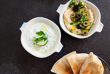 Tzatziki sauce and hummus. Gray grunge background. Greek sauce made from yogurt and vegetables, traditional hummus with olives. Top view, flat lay, copy space