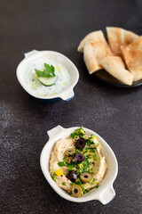 Tzatziki sauce and hummus. Gray grunge background. Greek sauce made from yogurt and vegetables, traditional hummus with olives. Top view, flat lay, copy space