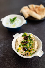 Tzatziki sauce and hummus. Gray grunge background. Greek sauce made from yogurt and vegetables, traditional hummus with olives. Top view, flat lay, copy space