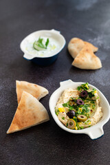 Tzatziki sauce and hummus. Gray grunge background. Greek sauce made from yogurt and vegetables, traditional hummus with olives. Top view, flat lay, copy space