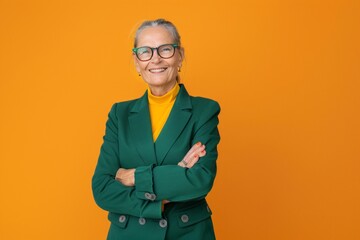 Fototapeta premium Full body elderly smiling happy cool confident woman 50s in green classic suit hold hands crossed folded isolated on plain orange color background studio portrait. People business lifestyle concept