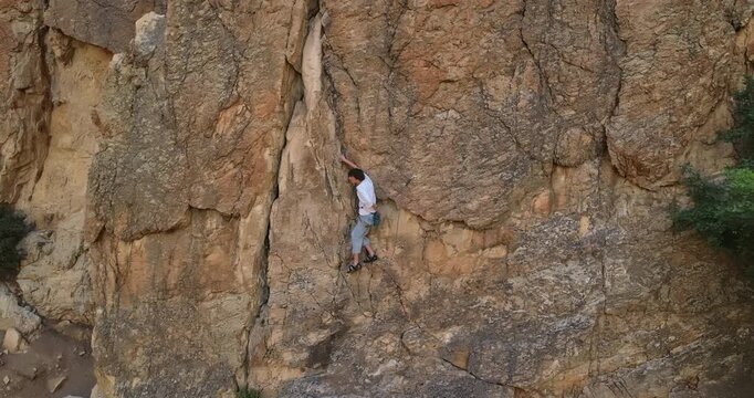 Young rock climber on side of beautiful mountain - drone moving out for wider shot