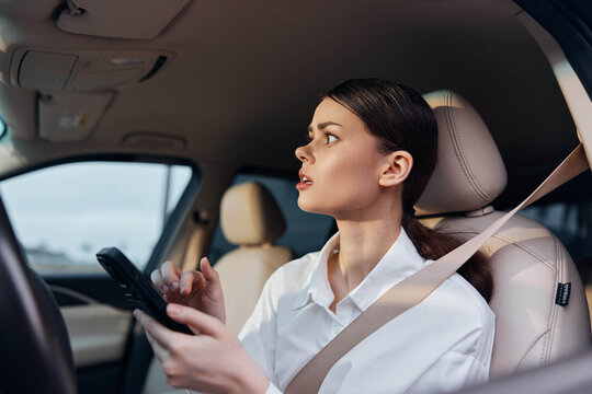 Woman in car driver's seat holding phone, intently looking at screen, demonstrating use of mobile technology while driving, emphasizing the importance of staying connected and potential distracted