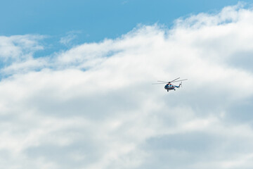 A civil aviation helicopter MI-8 in white, red and blue colors flying in the sky with clouds