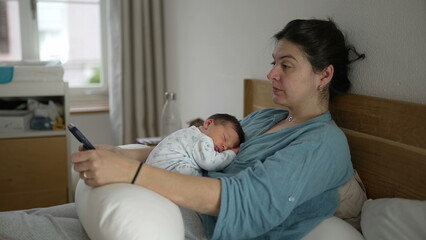 Fototapeta premium Tired mother with newborn baby sleeping on her chest, rubbing her eyes while holding a smartphone, wearing comfortable clothing, intimate indoor setting, showing exhaustion and love