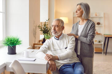 Obraz premium Portrait of calm peaceful senior woman hugging elderly man sitting at home. Mature married couple looking at the window enjoying being together. Relationship in retirement concept.