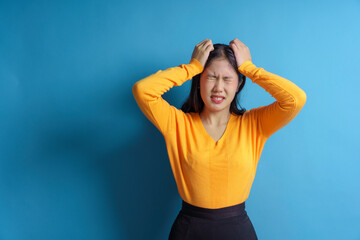 Stressed woman pulling hair, feeling frustrated and overwhelmed, with a blue background showing...