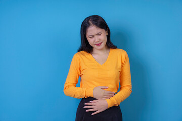 Young woman wearing a yellow sweater is holding her belly and suffering from strong stomach pain