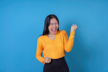 Fototapeta premium Young woman is shouting with joy, celebrating a success with enthusiasm while raising her fists in the air