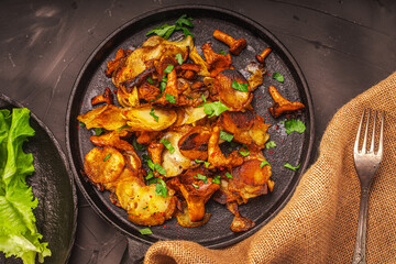 Chanterelles fried with potatoes according to a traditional recipe in a cast-iron pan on a dark background with a canvas napkin, tomatoes, lingonberries and herbs.