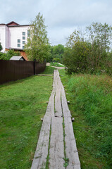 Old long wooden sidewalk on green grass in Soligalich town, Kostroma region, Russia