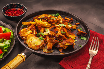Chanterelle mushrooms fried with potatoes according to a traditional recipe in a cast-iron pan on a dark table with a burgundy napkin, with vegetables and berries